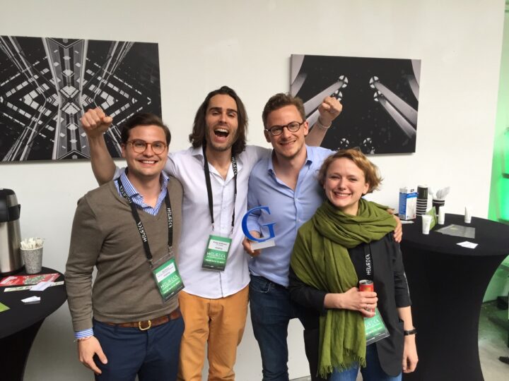 Vier Personen lächeln, halten Trophäe, im Hintergrund abstrakte Kunstwerke. Reinigungskraft.